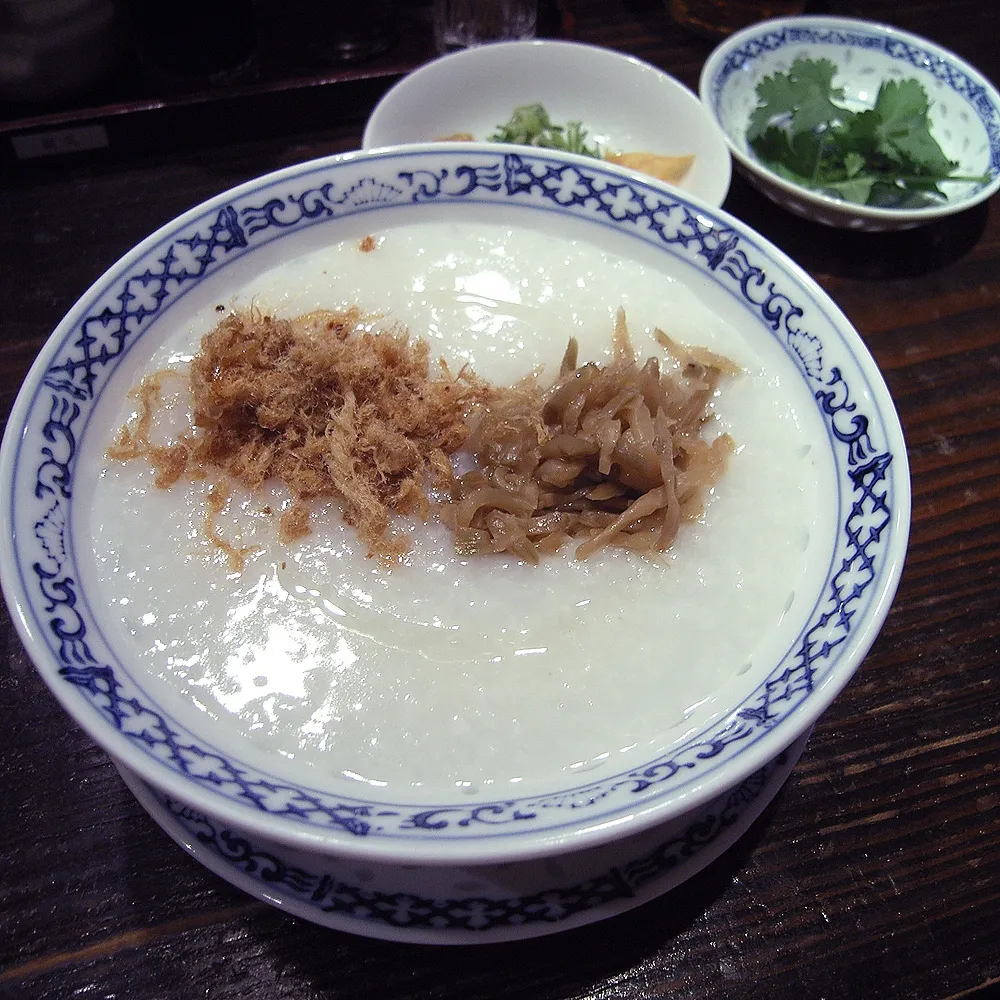 A bowl of plain Chinese rice congee topped with preserved vegetables and pork floss