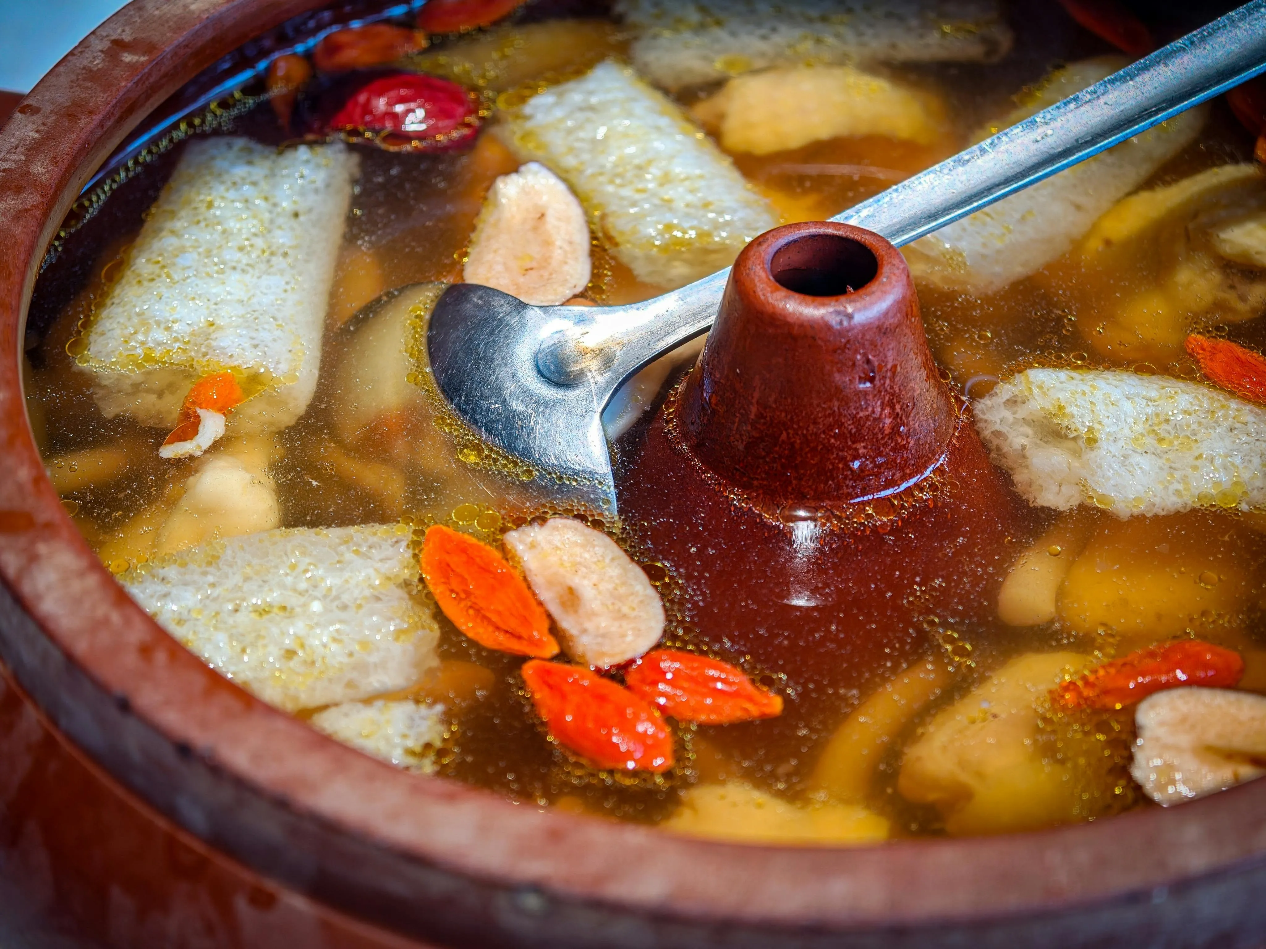 A clay-pot soup with goji berries and herbs simmering in a copper hotpot