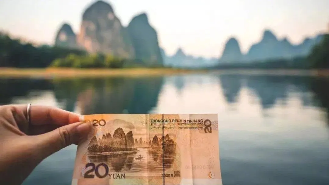 A ¥20 note held up against the real Li River peaks near Xingping — the exact scene printed on the back of the banknote