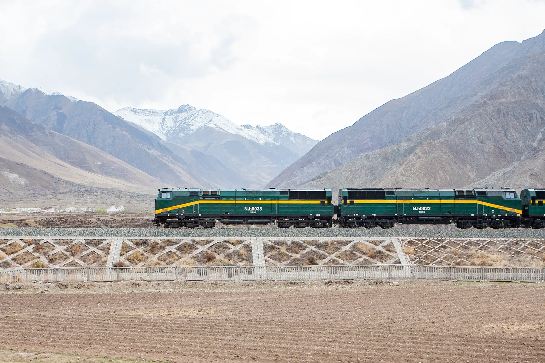 A Qinghai–Tibet Railway train hauled by twin green locomotives crossing the high plateau below snow-capped mountains near Lhasa