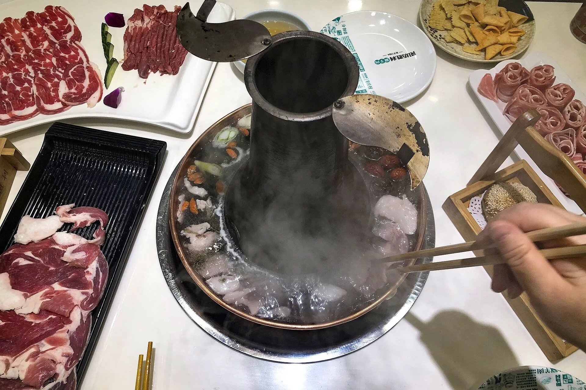 A copper-chimney pot of Beijing instant-boiled mutton, steaming, with plates of thin lamb slices