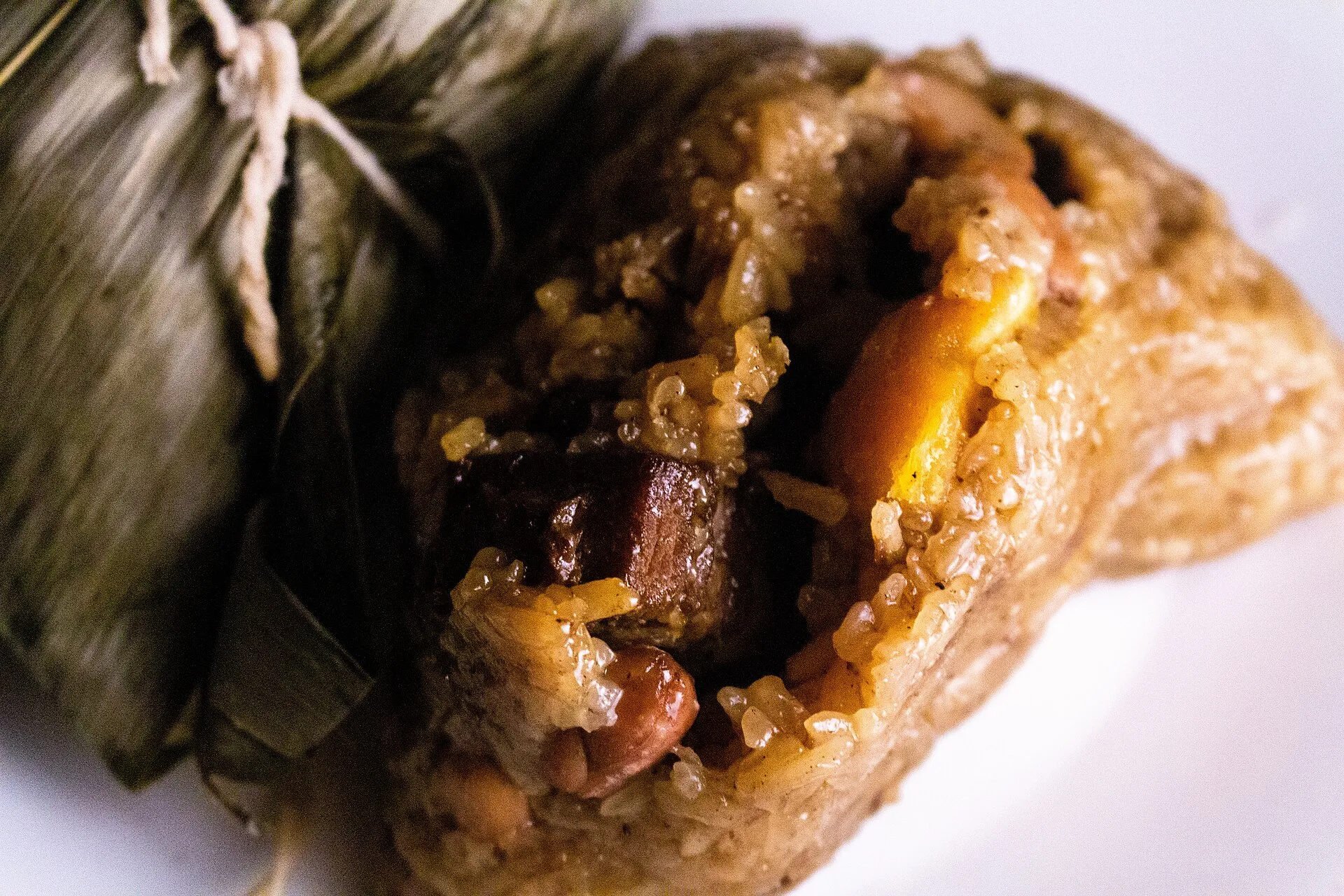 An opened savoury zongzi showing sticky rice, pork and salted egg yolk, beside a wrapped one