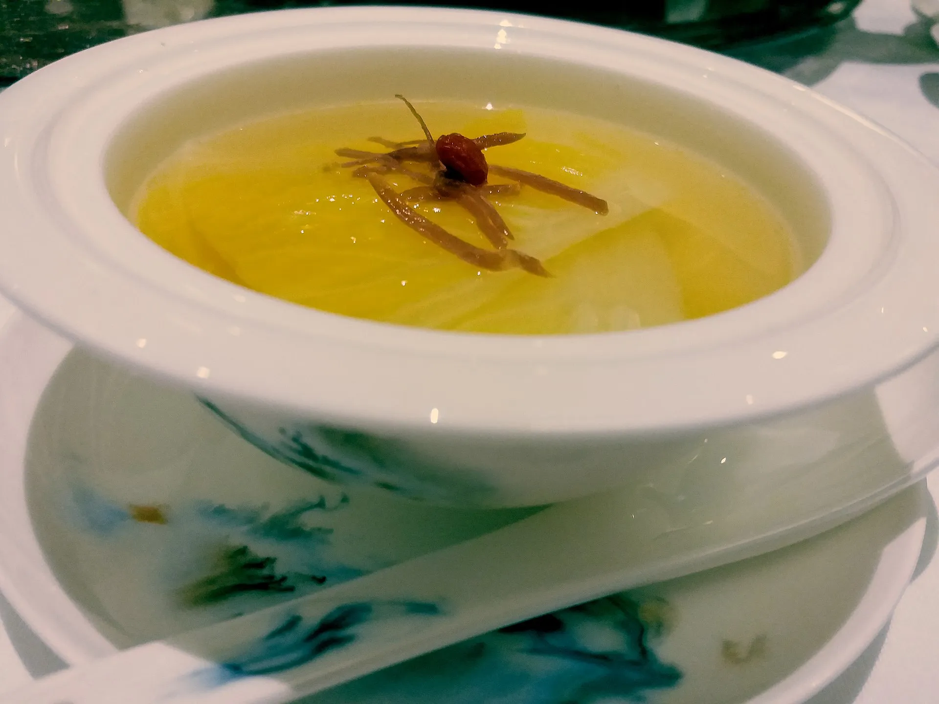 Boiling-water cabbage — pale cabbage hearts arranged like a blossom, topped with a goji berry, in a clear consommé